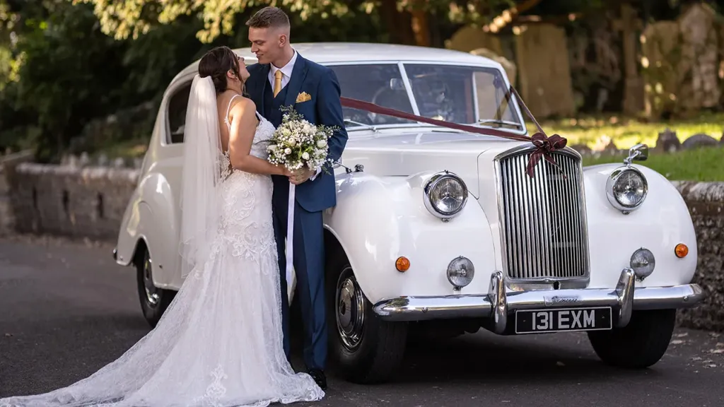 Nride and Groom standing by the Austin Princess Limousine in front of a church