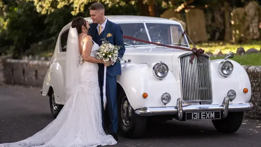 Nride and Groom standing by the Austin Princess Limousine in front of a church