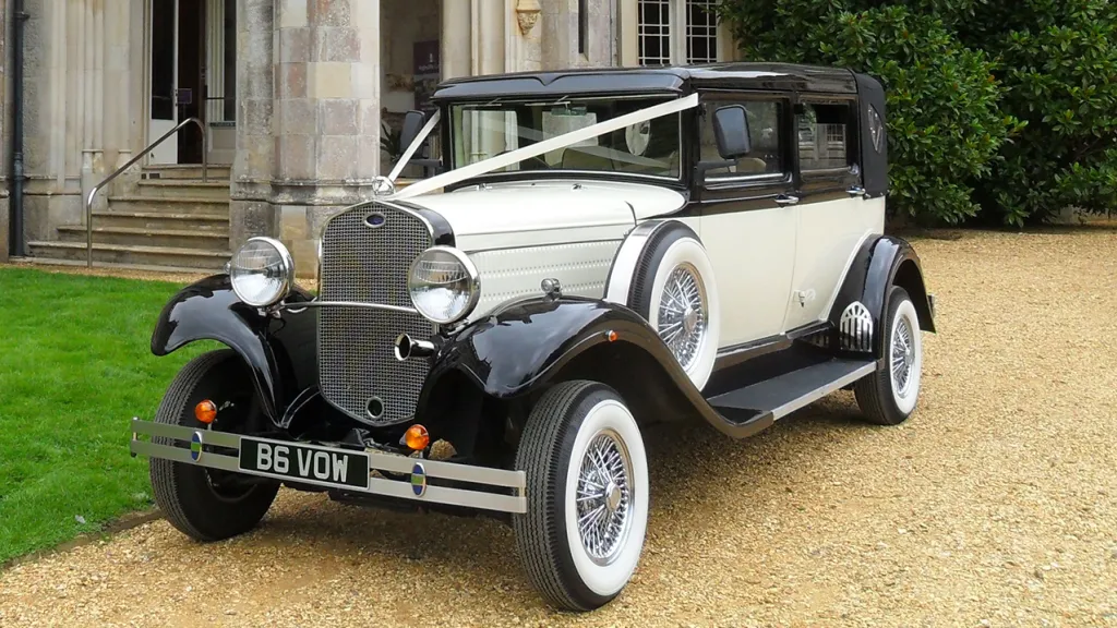 Front side view of Ivory Vintage Branford car with  Black Roof and Black Wheel Arches dressed with White Ribbons in front of wedding venue in Scunthorpe