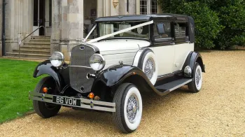 Front side view of Ivory Vintage Branford car with  Black Roof and Black Wheel Arches dressed with White Ribbons in front of wedding venue in Scunthorpe
