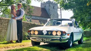 Classic Ivory Stag decorated with white ribbons. Bride and Groom standing by the vehicle