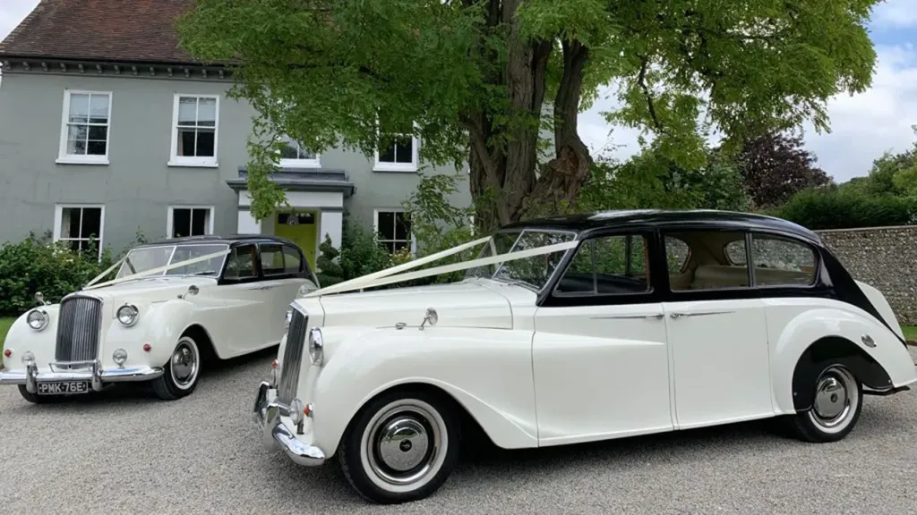Two Classic Asutin standing next to each others decorated with white wedding ribbons in front of wedding venue