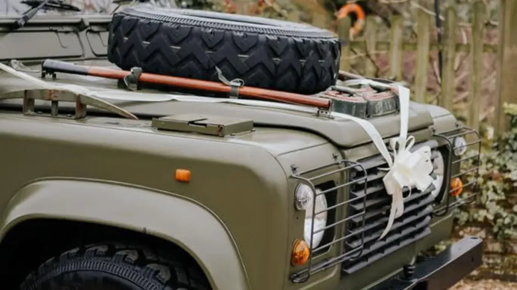 White Ribbon and bow on the front grill of the Khaki Green Military Landrover Vehicle. Spare wheel mounted on bonnet