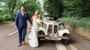 Brde and Groom holding hands while walking in front of a Beauford Wedding Car.
