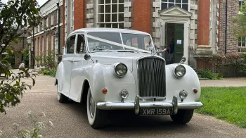 Front view of Classic Austin Princess decorated with white ribbons across its bonnet leaving a wedding venue in Essex