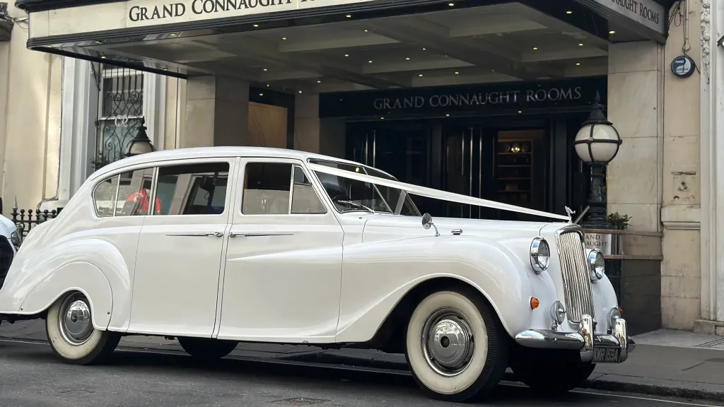 Side view of Classic Austin princess decorated with white wedding ribbons waiting outside Grand Connaught Hotel in London