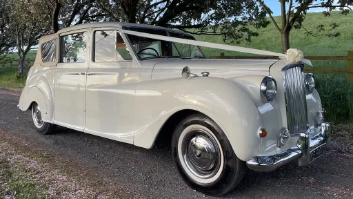 Convertible Classic austin Princess with White Ribbons across the front bonnet. Cream Soft-Top Roof is up.