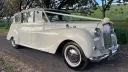 Convertible Classic austin Princess with White Ribbons across the front bonnet. Cream Soft-Top Roof is up.