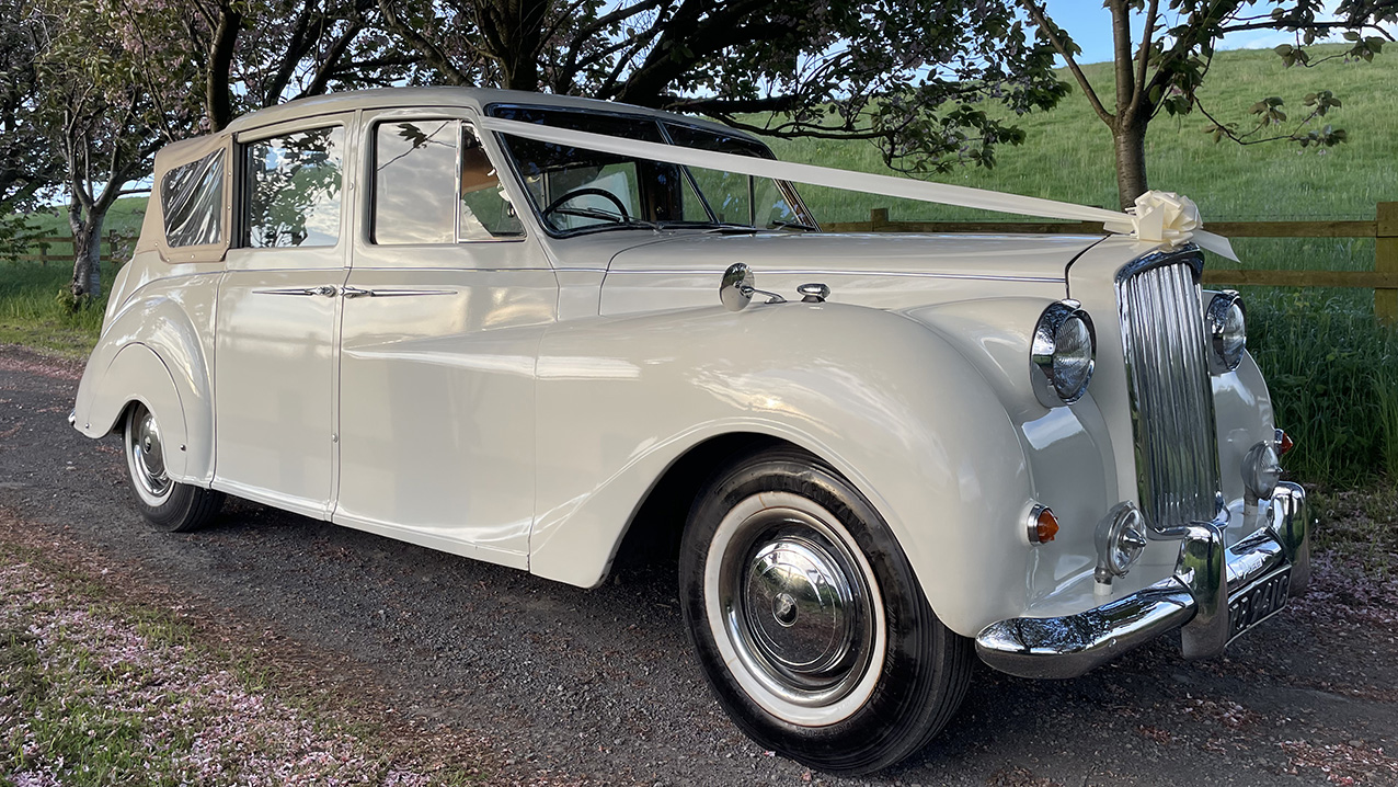 Convertible Classic austin Princess with White Ribbons across the front bonnet. Cream Soft-Top Roof is up.