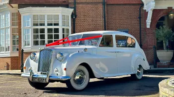 Front Left side view of classic Austin Princess Limousine decorated with red Ribbons in front of Wedding venue