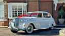 Front Left side view of classic Austin Princess Limousine decorated with red Ribbons in front of Wedding venue
