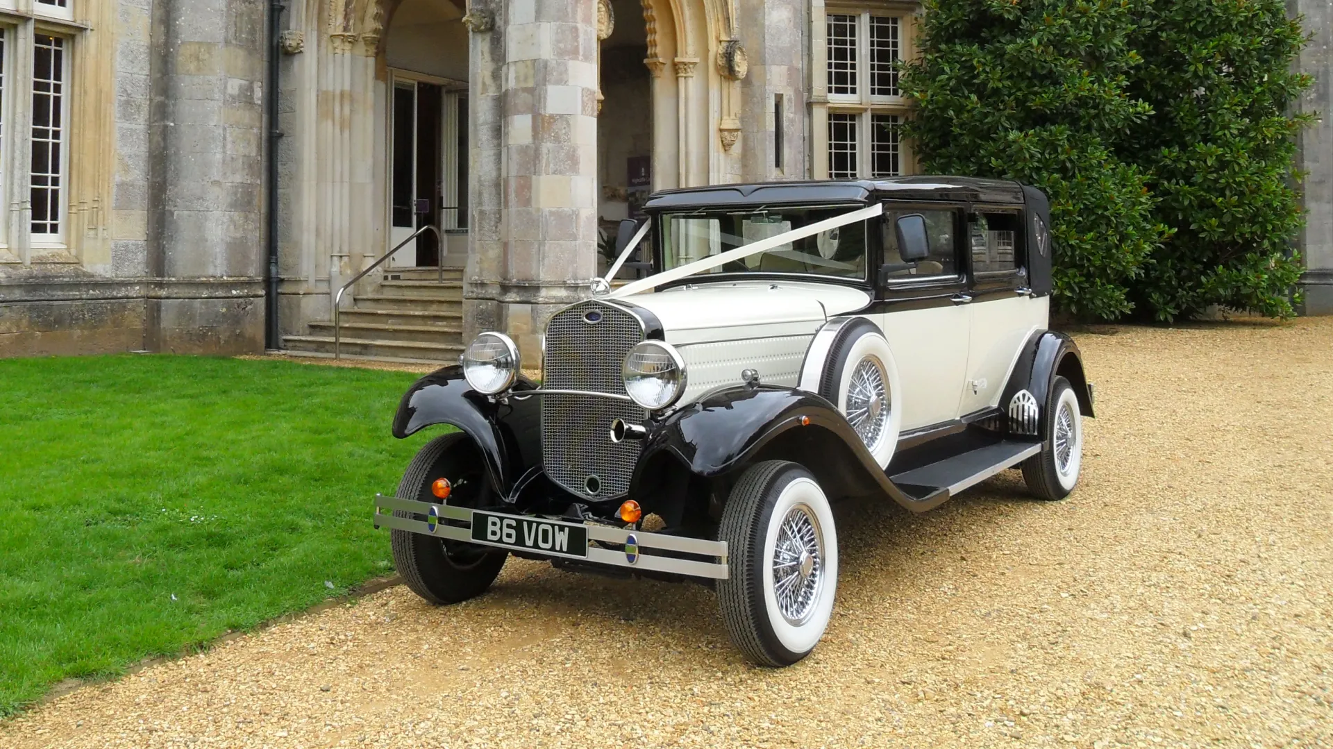 Black and Ivory Convertible Vintage Wedding Car Limousine decorated with ribbons with Wedding Venue in the background