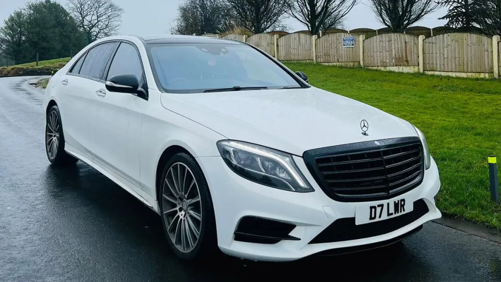 Front Side view of White Mercedes S-class parked on a road showing large Mercedes Grill and Chrome Alloy Wheels