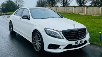 Front Side view of White Mercedes S-class parked on a road showing large Mercedes Grill and Chrome Alloy Wheels