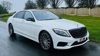 Front Side view of White Mercedes S-class parked on a road with green grass in the background