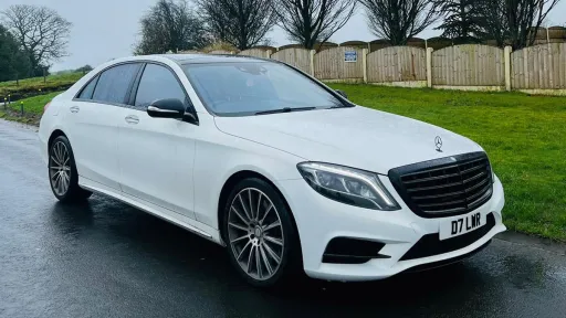 Front Side view of White Mercedes S-class parked on a road with green grass in the background