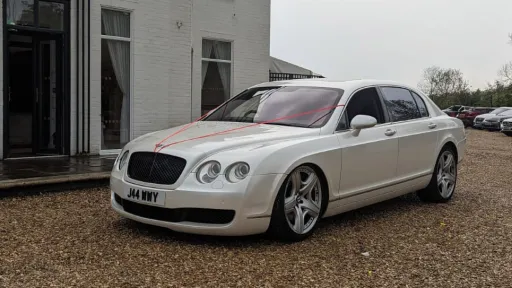 Left Side View of White Bentley Flying spare decorated with a thin Red Ribbon accross its bonnet.