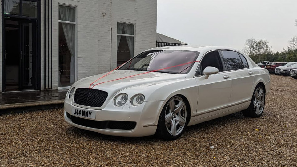 Left Side View of White Bentley Flying spare decorated with a thin Red Ribbon accross its bonnet.