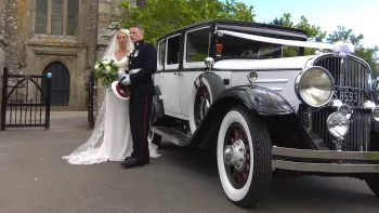 Bride wearing a white dress and Groom wearing Army unform standing side-by-side next to an American vintage Franklin dressed with white ribbons