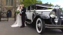 Bride wearing a white dress and Groom wearing Army unform standing side-by-side next to an American vintage Franklin dressed with white ribbons