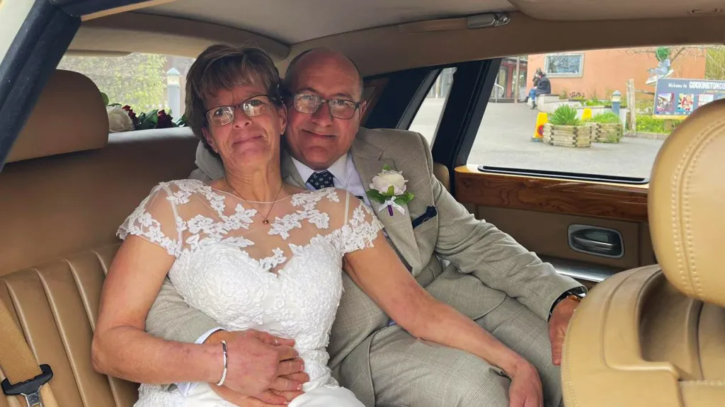 Bride and Groom seating in the rear of the Rolls-Royde phantom looking towards the photograher while holding each other.