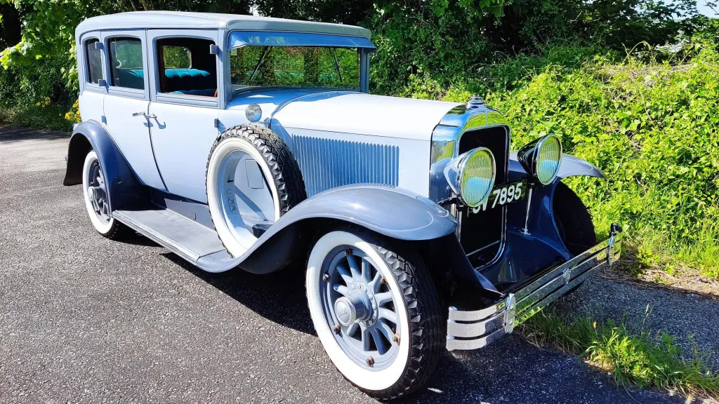 Silver and Grey vintage Buick Master Sedan parked in front of a green hay