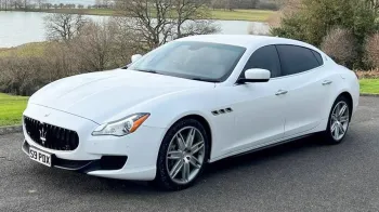 Front side view of white Maserati white privacy windows at the rear parked in a park with a lac in the background