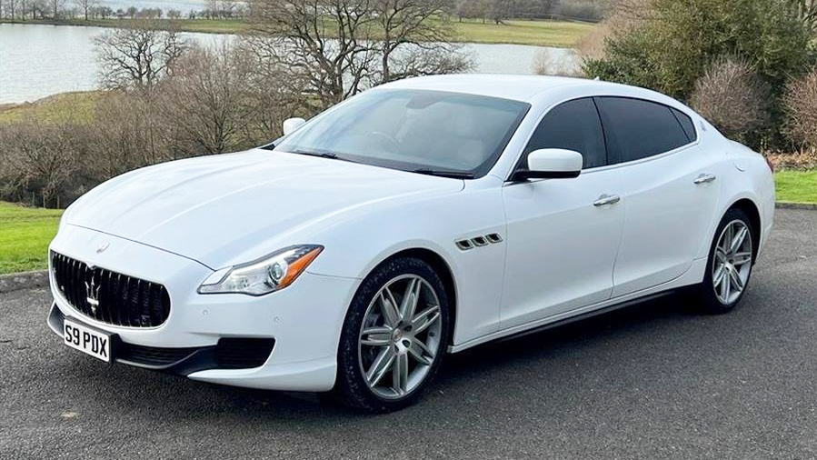 Front side view of white Maserati white privacy windows at the rear parked in a park with a lac in the background