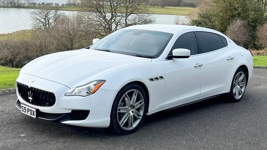 Front side view of white Maserati white privacy windows at the rear parked in a park with a lac in the background