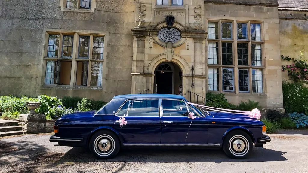 Right side view of blue crols-royce with ribbons and bows in front of a wedding venue
