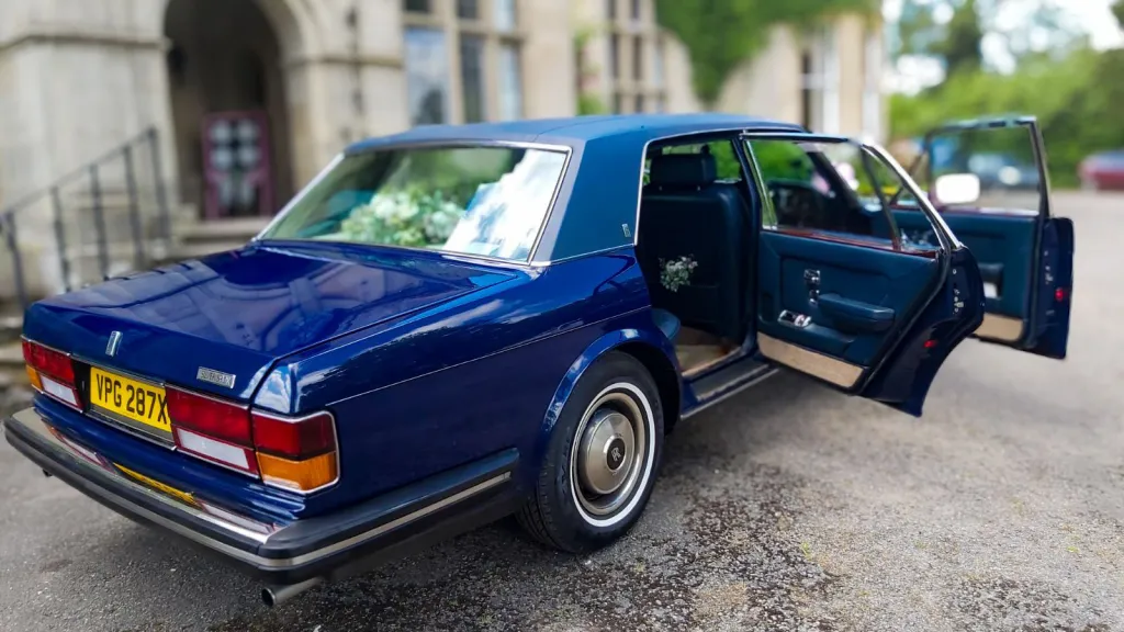 Side rear view of blue classic rolls-royce with both front and rear doors open showing blue interior on door panels
