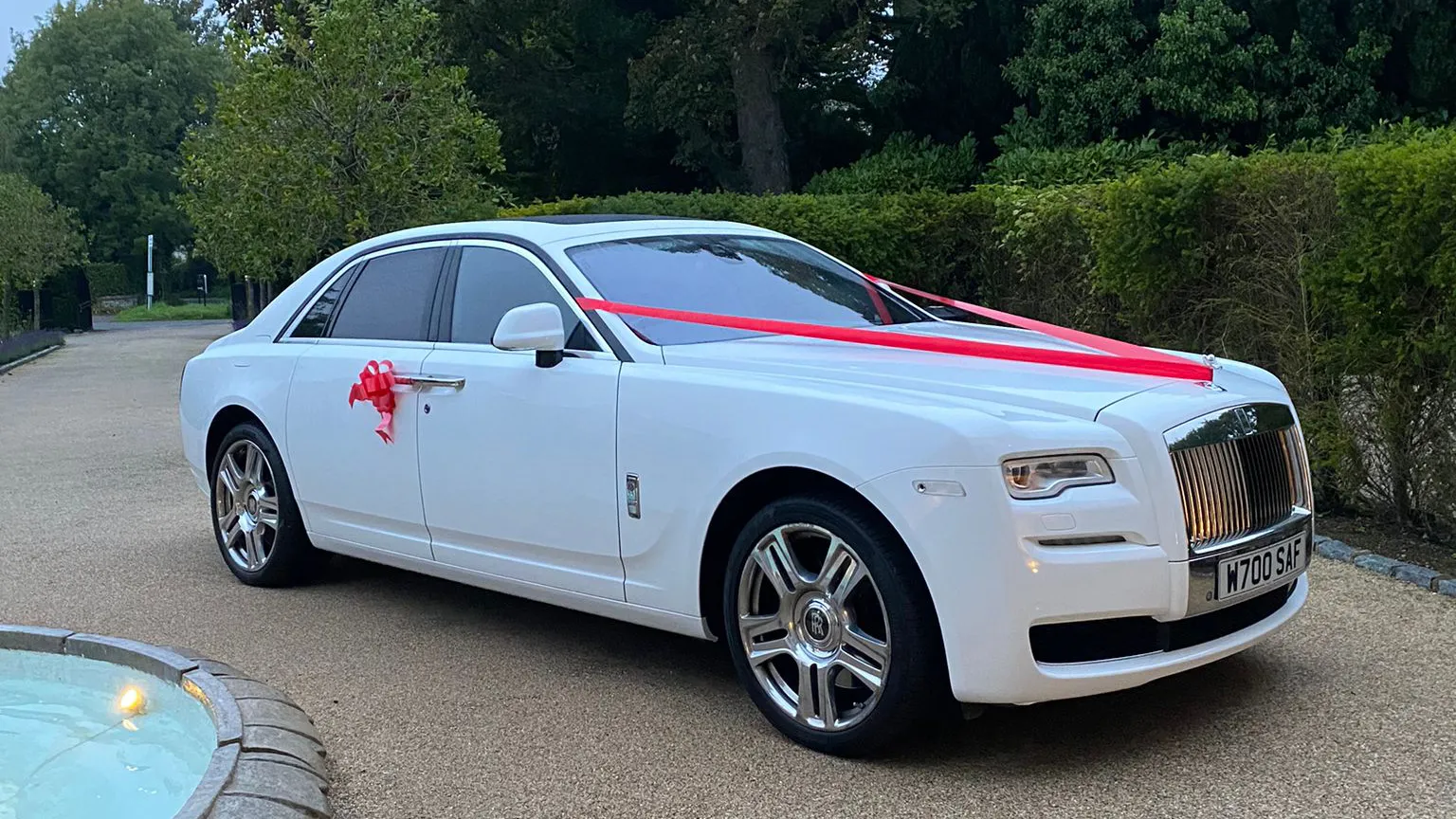 A modern white Rolls-Royce Ghost with Red Ribbons and bows on its door handle in Walton-on-Thames.
