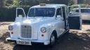 Front view of white classic taxi cab with Orange taxi sign at the top and rear-hinged doors open.