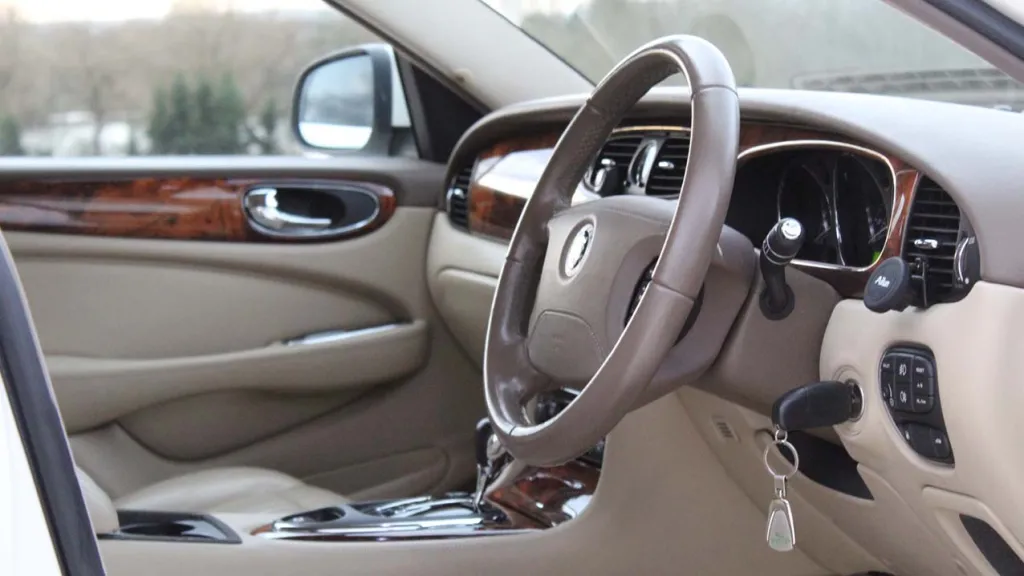 Front interior view of white jaguar XJ with cream leather, wooden door panel and dashboard