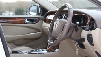 Front interior view of white jaguar XJ with cream leather, wooden door panel and dashboard