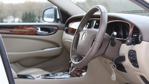 Front interior view of white jaguar XJ with cream leather, wooden door panel and dashboard