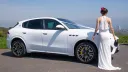 Right Side view of White Maserati Grecale with white ribbons accross its bonnet and Bride wearing a white dress