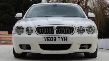 Full front view of white Jaguar XJ with twein headligs and Jaguar badge in the middle of the grill