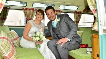 Bride and Groom seating inside the campervan's rear seating area showing a green cloth seats with cushions and curtains on the windows