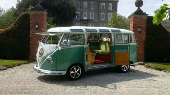 Left side view of Classic campervan in white and pale green in front of a wedding venue in devon with rear doors open