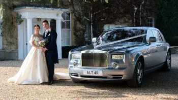 Bride and Groom holding each others in front of their wedding venue with Modern Rolls-Royce Phantom in silver dressed with ribbons on the side