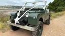 Front Left view of an Army Green Land Rover Series 1 decorated with White Ribbons and bows. Devon coastline can be seen in the background
