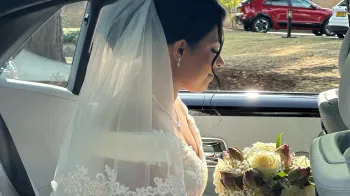 Bride holding a white rosed bouquet of flowers sitting inside car