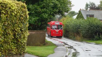 Vintage single decker red bus driving through the Buckinghamshire countryroads