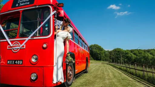 Bride and Groom kissing on the door step of a vintage red bus