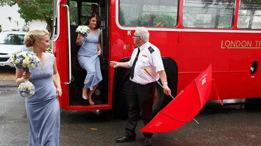 Bridesmaids wearing a light purple dress stepping out of a vintage bus with help from chauffeur
