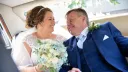 Bride and her father inside Classic Limousine. Bride is holding a large bouquet of flowers and smiling at her dad.