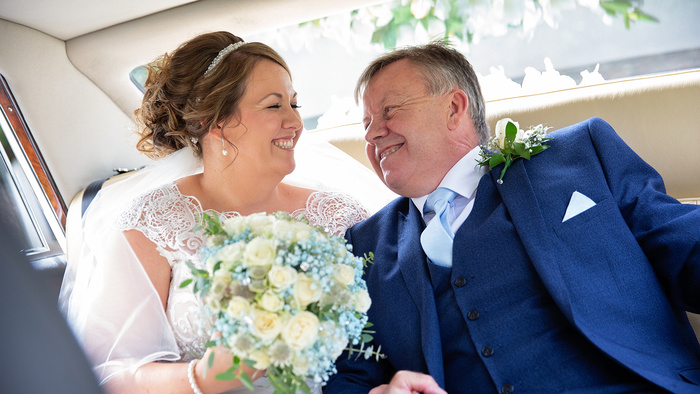 Bride and her father inside Classic Limousine. Bride is holding a large bouquet of flowers and smiling at her dad.