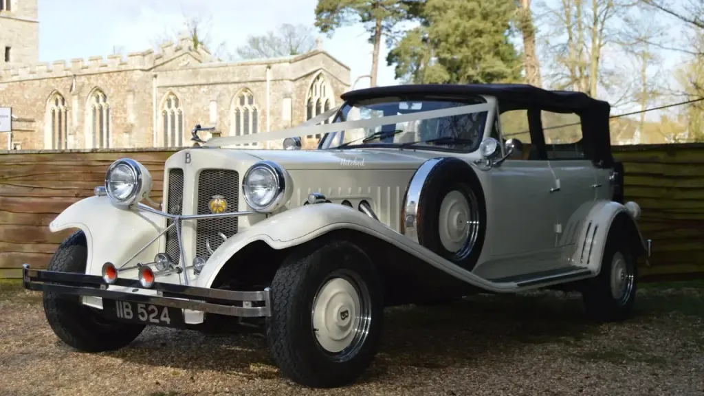ivory vintage Beauford decorated white ribbons, black soft-top roof and spare wheel mounted on the side of the vehicle