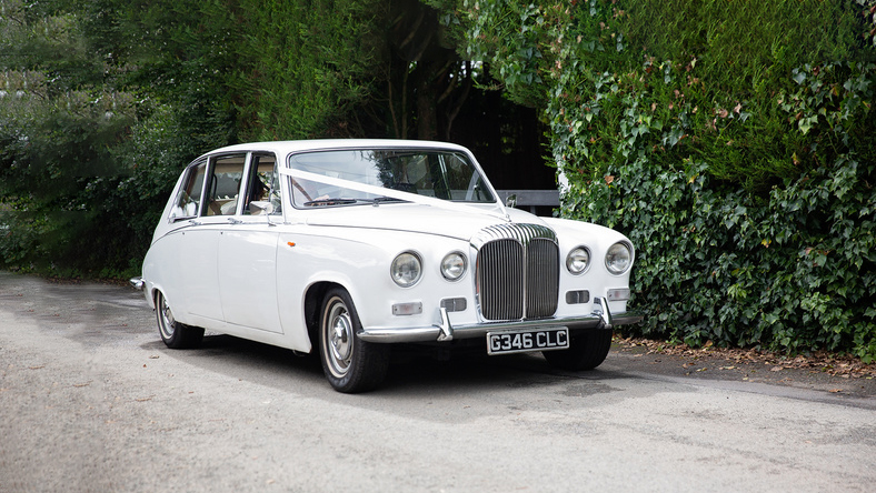 White 7-seater Classic Daimler Limousine decorated with ribbons entering wedding venue